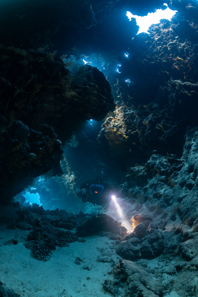 Rebreather diver in a cave passage with light holes in the ceiling, Saint John's Cave, Red Sea, Egypt