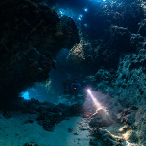 Rebreather diver lighting the sculpted cave wall, Saint John's Cave, Red Sea, Egypt