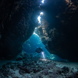 Distant rebreather diver below a chain of skylights, Saint John's Cave, Red Sea, Egypt