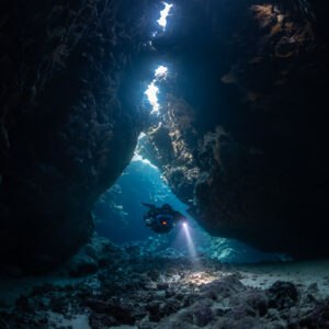 Rebreather diver approaching below a chain of skylights, Saint John's Cave, Red Sea, Egypt