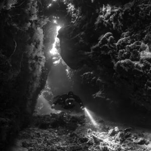 Rebreather diver in a cave fissure under skylights, black and white, Saint John's Cave, Red Sea, Egypt