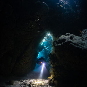 Rebreather diver far away in a glowing cave doorway, Saint John's Cave, Red Sea, Egypt