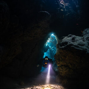 Rebreather diver framed in a glowing cave doorway, Saint John's Cave, Red Sea, Egypt