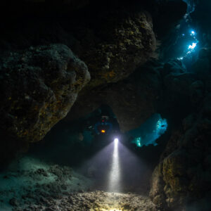 Rebreather diver emerging between boulders in the dark cave, Saint John's Cave, Red Sea, Egypt