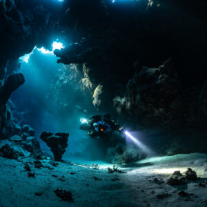 Rebreather diver crossing a sandy cave hall lit by sunbeams, Saint John's Cave, Red Sea, Egypt