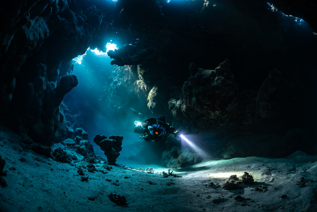 Rebreather diver crossing a sandy cave hall lit by sunbeams, Saint John's Cave, Red Sea, Egypt