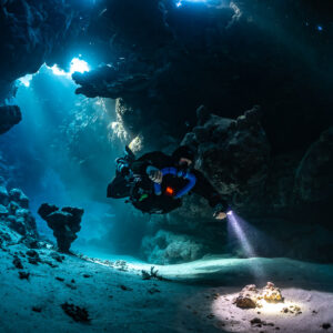Rebreather diver close to the camera in a sunlit cave hall, Saint John's Cave, Red Sea, Egypt