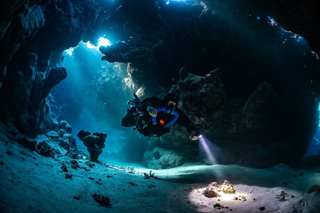 Rebreather diver close to the camera in a sunlit cave hall, Saint John's Cave, Red Sea, Egypt
