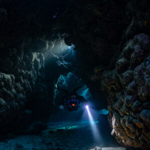 Rebreather diver in a side gallery, torch on the sand, Saint John's Cave, Red Sea, Egypt