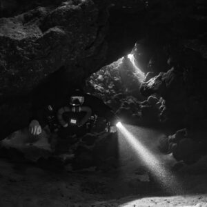 Rebreather diver under a low cave ceiling, black and white, Saint John's Cave, Red Sea, Egypt