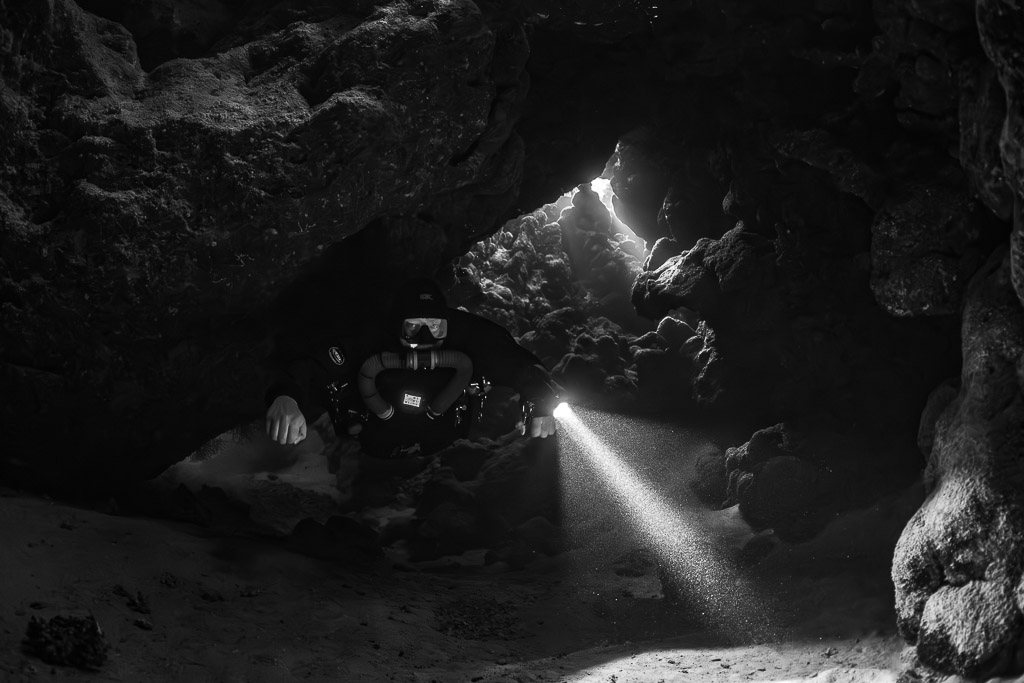 Rebreather diver under a low cave ceiling, black and white, Saint John's Cave, Red Sea, Egypt