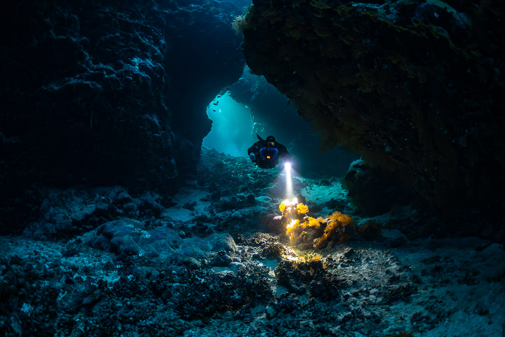 Rebreather diver lighting an orange sponge at a cave opening, Saint John's Cave, Red Sea, Egypt