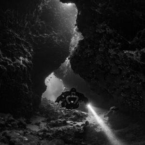 Rebreather diver in a winding cave passage, black and white, Saint John's Cave, Red Sea, Egypt