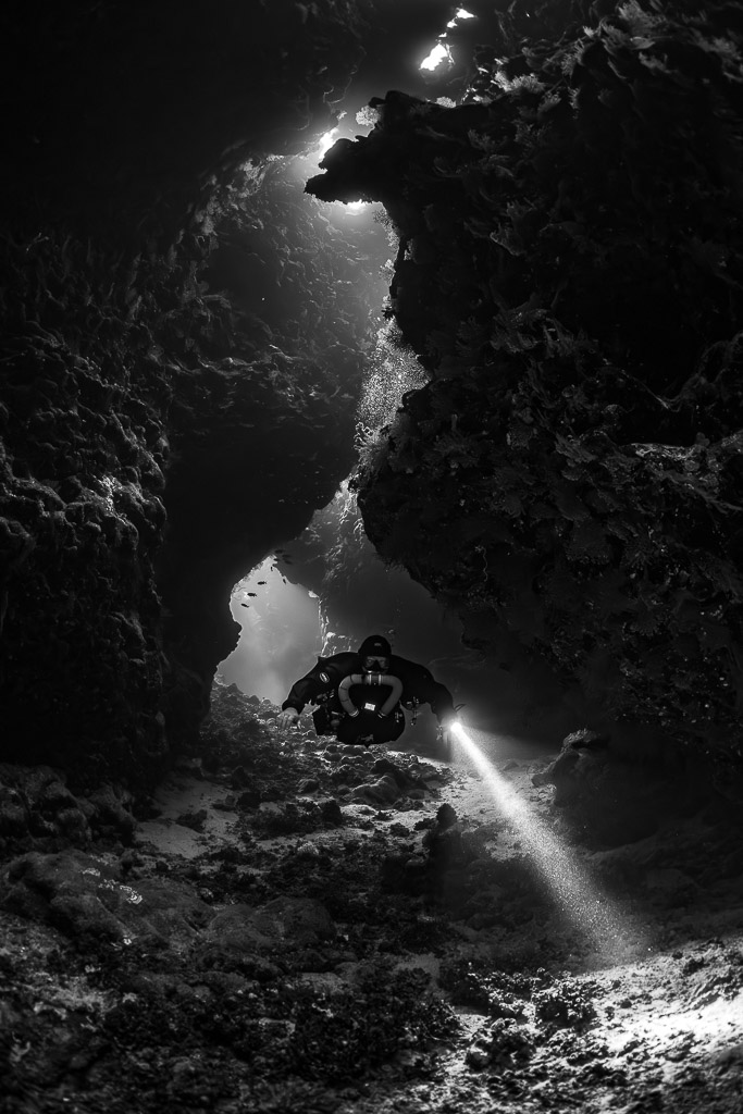Rebreather diver in a winding cave passage, black and white, Saint John's Cave, Red Sea, Egypt