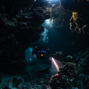 Rebreather diver close-up in the cave, torch on a red sponge, Saint John's Cave, Red Sea, Egypt