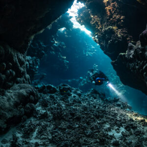 Rebreather diver in a cave gallery beneath a long light slit, Saint John's Cave, Red Sea, Egypt