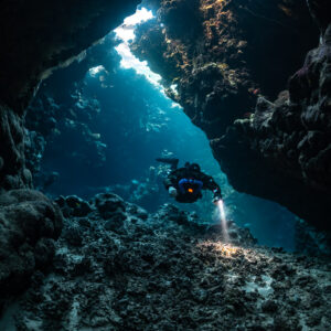 Rebreather diver below a long light slit in the cave roof, Saint John's Cave, Red Sea, Egypt