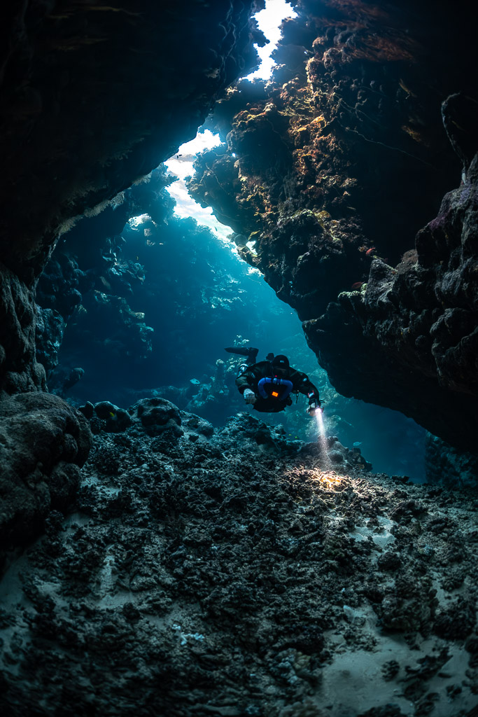 Rebreather diver below a long light slit in the cave roof, Saint John's Cave, Red Sea, Egypt