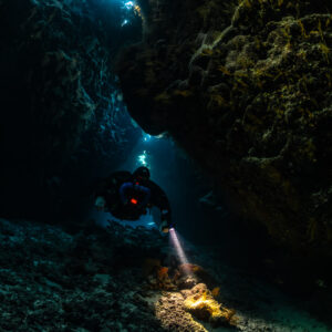 Rebreather diver closer in a low dark cave chamber, Saint John's Cave, Red Sea, Egypt