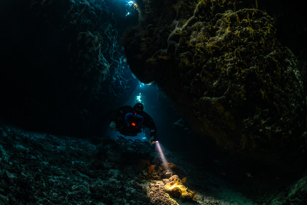 Rebreather diver closer in a low dark cave chamber, Saint John's Cave, Red Sea, Egypt