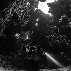 Rebreather diver below a large cave skylight, black and white, Saint John's Cave, Red Sea, Egypt