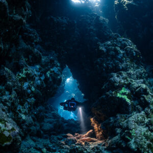 Distant rebreather diver in a cave arch below skylights, Sha'ab Claudio, Red Sea, Egypt