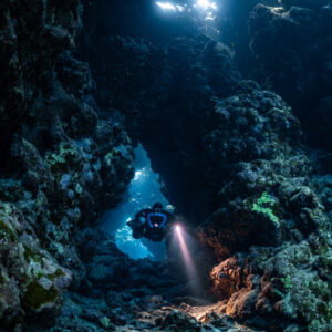 Rebreather diver in a cave arch, torch on orange sponge, Sha'ab Claudio, Red Sea, Egypt