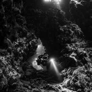 Rebreather diver in a cave arch below skylights, black and white, Sha'ab Claudio, Red Sea, Egypt