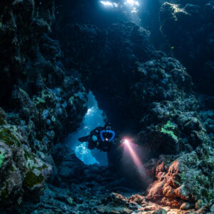Rebreather diver lighting an orange sponge at a cave arch, Sha'ab Claudio, Red Sea, Egypt