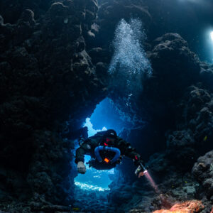 Rebreather diver passing through a cave arch with exhaled bubbles rising, Sha'ab Claudio, Red Sea, Egypt