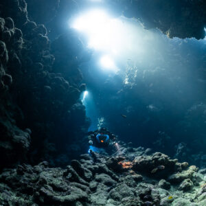 Small rebreather diver under a blaze of light in the cave, Sha'ab Claudio, Red Sea, Egypt