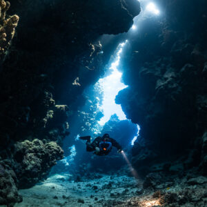 Rebreather diver entering a light-filled fissure, Sha'ab Claudio, Red Sea, Egypt