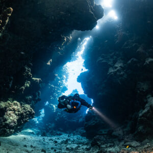 Rebreather diver in a light-filled fissure, torch beam on the sand, Sha'ab Claudio, Red Sea, Egypt