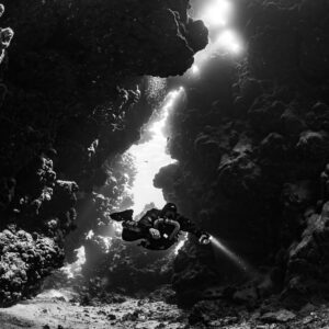 Rebreather diver in a light-filled fissure, black and white, Sha'ab Claudio, Red Sea, Egypt