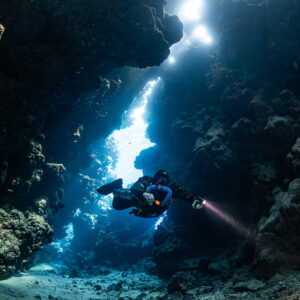 Rebreather diver close to the camera in a light-filled fissure, Sha'ab Claudio, Red Sea, Egypt