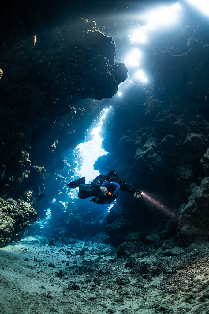 Rebreather diver close to the camera in a light-filled fissure, Sha'ab Claudio, Red Sea, Egypt