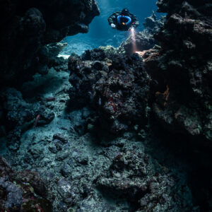 Rebreather diver high in a blue cave window, rubble below, Sha'ab Claudio, Red Sea, Egypt