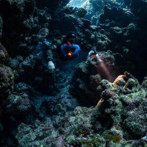 Rebreather diver coming down a dark cave passage with torch, Sha'ab Claudio, Red Sea, Egypt
