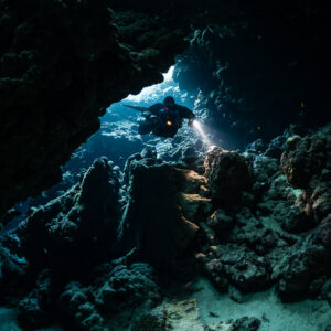 Rebreather diver framed by a blue opening at the back of the cave, Sha'ab Claudio, Red Sea, Egypt