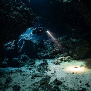 Rebreather diver below a skylight, torch spot on the sandy floor, Sha'ab Claudio, Red Sea, Egypt