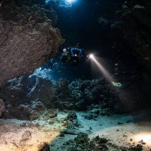 Rebreather diver between rock slabs, warm torch light on the sand, Sha'ab Claudio, Red Sea, Egypt