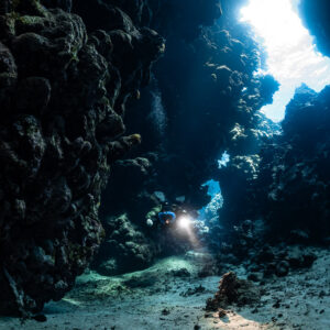 Small rebreather diver beside a tall bright fissure, Sha'ab Claudio, Red Sea, Egypt