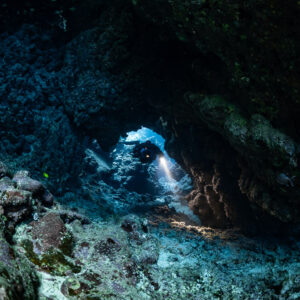 Rebreather diver in a low passage leading to a blue window, Sha'ab Claudio, Red Sea, Egypt