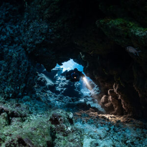 Rebreather diver framed by a small blue window in the cave, Sha'ab Claudio, Red Sea, Egypt