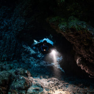 Rebreather diver lighting the cave floor beneath a small window, Sha'ab Claudio, Red Sea, Egypt