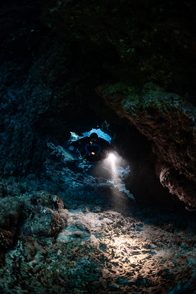 Rebreather diver lighting the cave floor beneath a small window, Sha'ab Claudio, Red Sea, Egypt