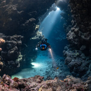 Rebreather diver in a sunbeam-lit gallery above pink encrusted rocks, Sha'ab Claudio, Red Sea, Egypt