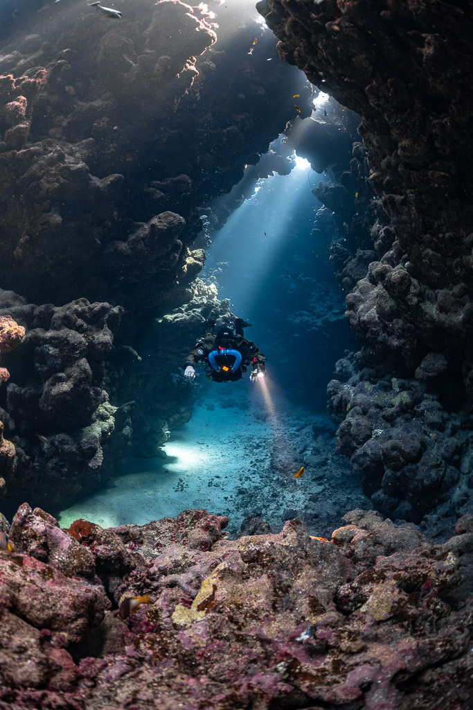 Rebreather diver in a sunbeam-lit gallery above pink encrusted rocks, Sha'ab Claudio, Red Sea, Egypt