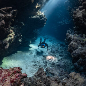 Rebreather diver in a narrow gallery under a single sunbeam, Sha'ab Claudio, Red Sea, Egypt