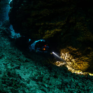 Rebreather diver lighting golden encrustations on the cave wall, Sha'ab Claudio, Red Sea, Egypt